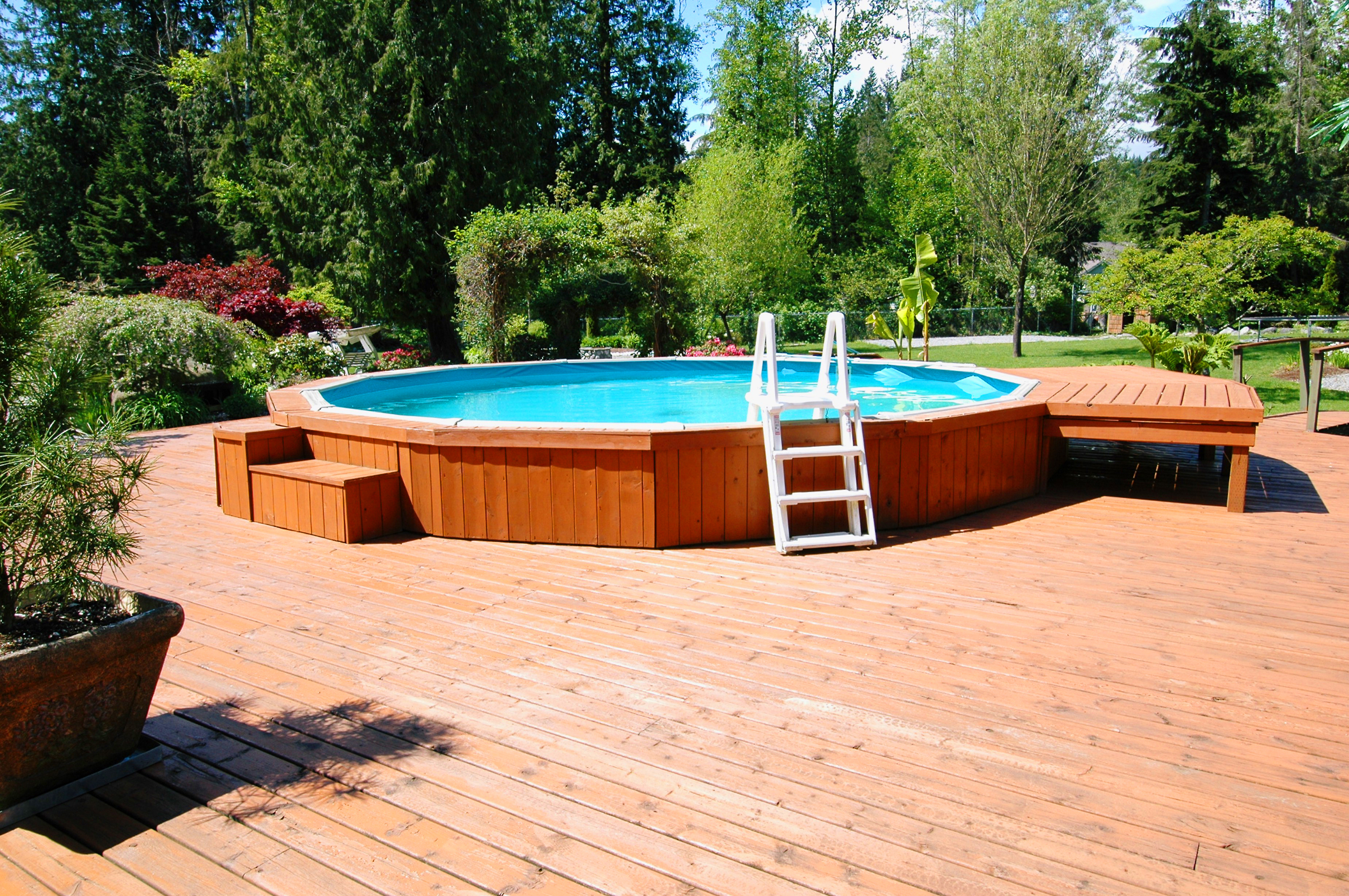 Above ground pool with a wooden deck and surrounding trees.