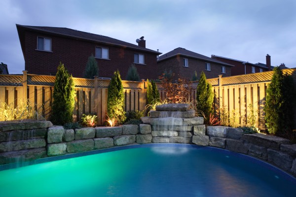 Backyard pool at night illuminated to highlight the pool and its surrounding landscaping.