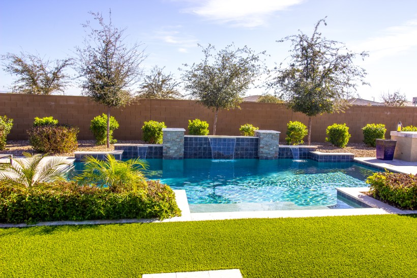 Modern, secluded swimming pool with waterfalls and surrounding plants in a backyard.