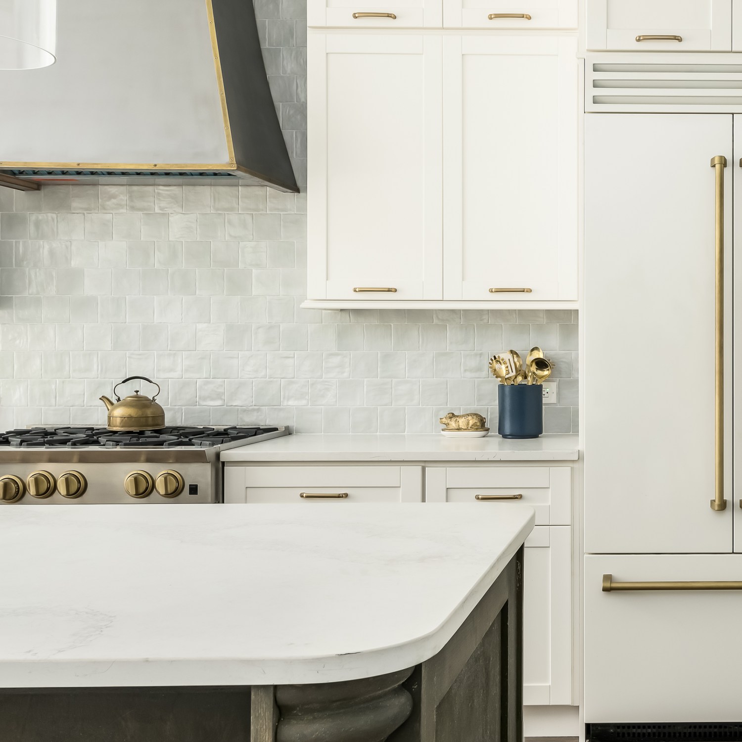 Elegant kitchen with a timeless white design, this kitchen features a white matte refrigerator, white cabinets, and two toned kitchen island with a gray tile backsplash.
