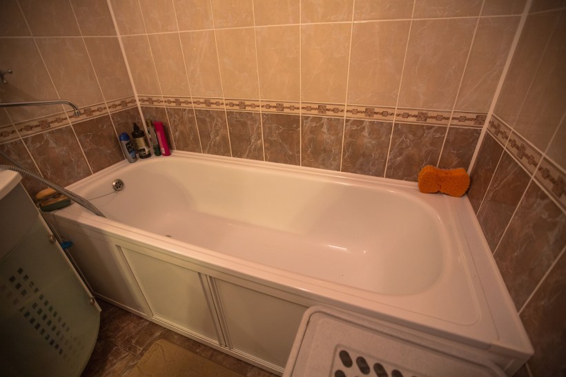 A white built-in bathtub with a shower and a sponge, shampoo, and other products on the sides.