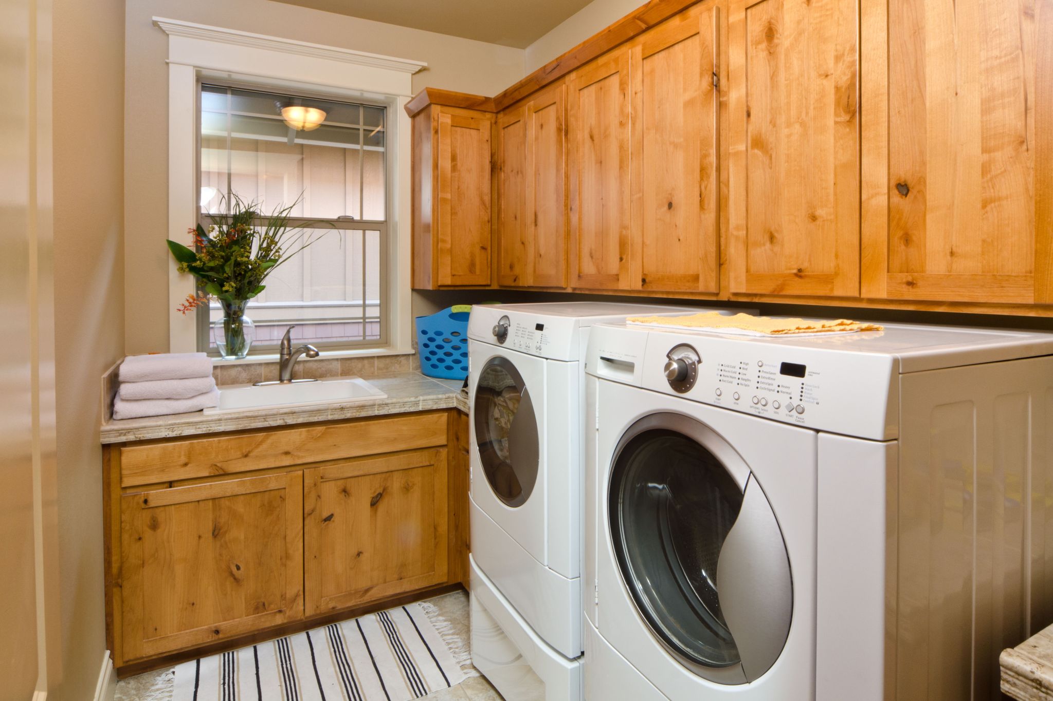 A modern laundry room with front loading washer and dryer and beautiful wood cabinets.