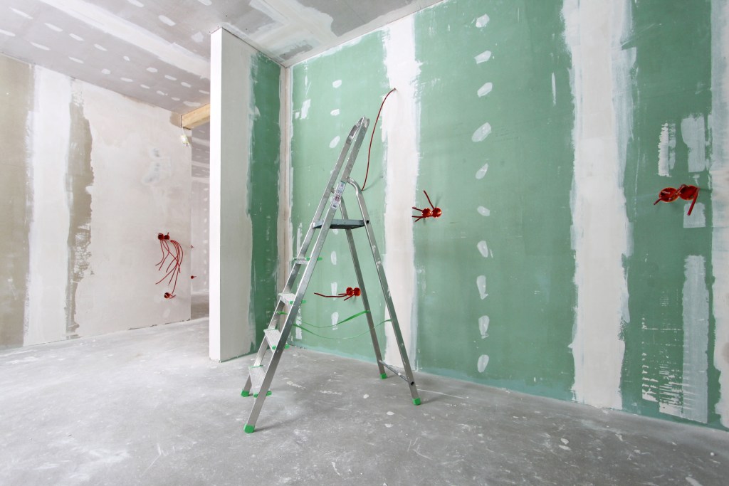 The inside of a room in a house under construction with drywall, ladders, and wiring.