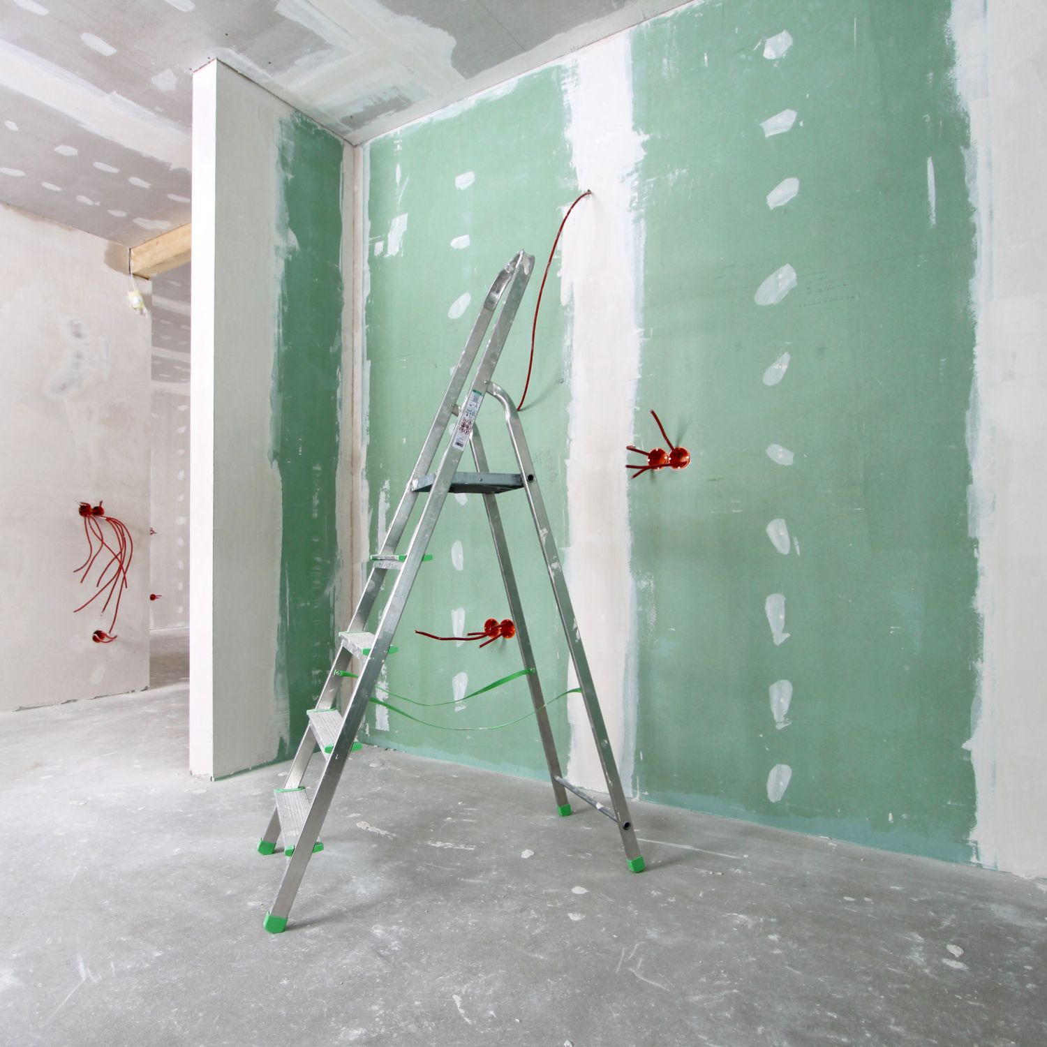 The inside of a room in a house under construction with drywall, ladders, and wiring.