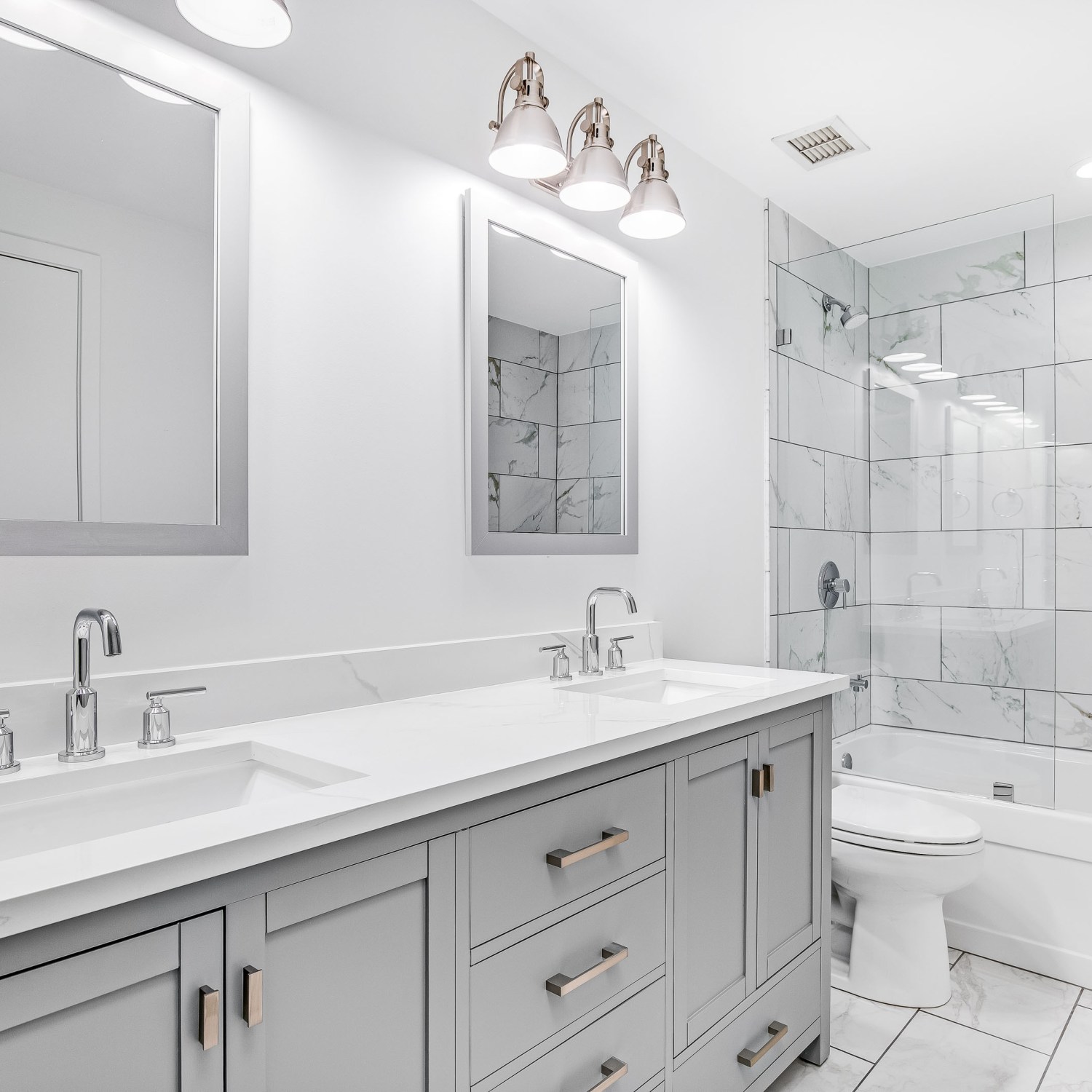An elegant, easy, clean remodeled bathroom with a grey vanity and bronze hardware.