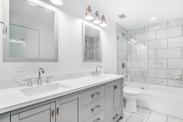 An elegant, easy, clean remodeled bathroom with a grey vanity and bronze hardware.