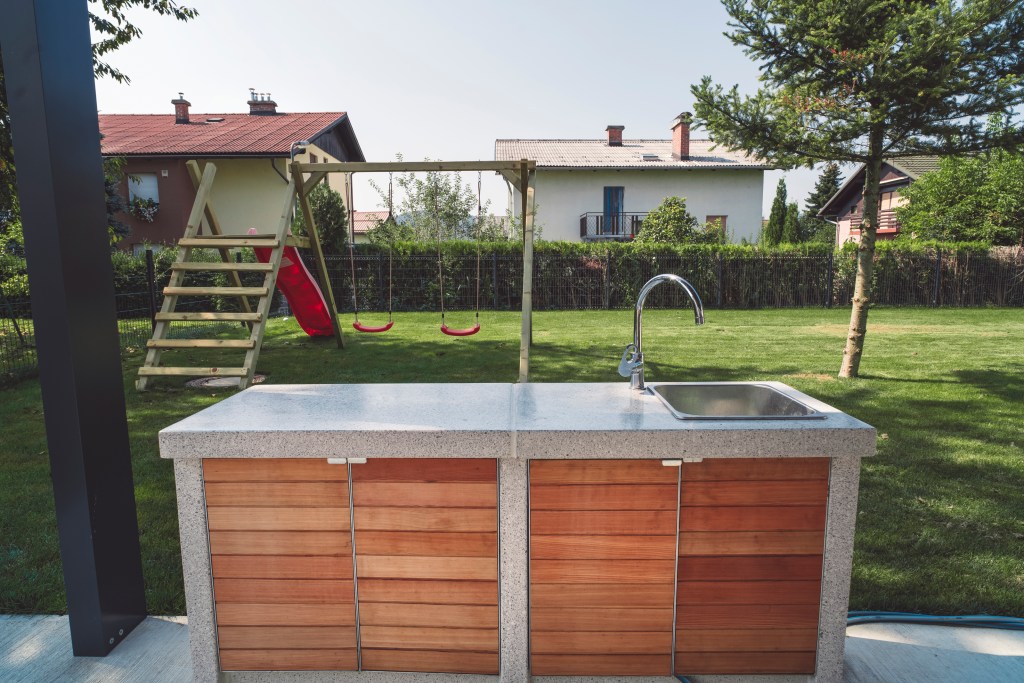 A beautiful sink sits outside as part of an outdoor kitchen under a pergola.