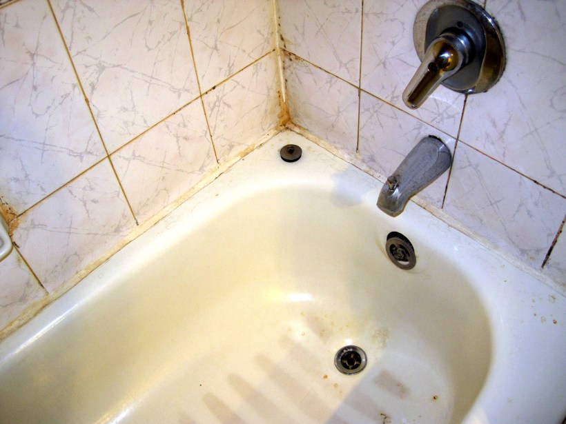 A dirty, rusty bathtub in bad condition that is in need of a refinishing.