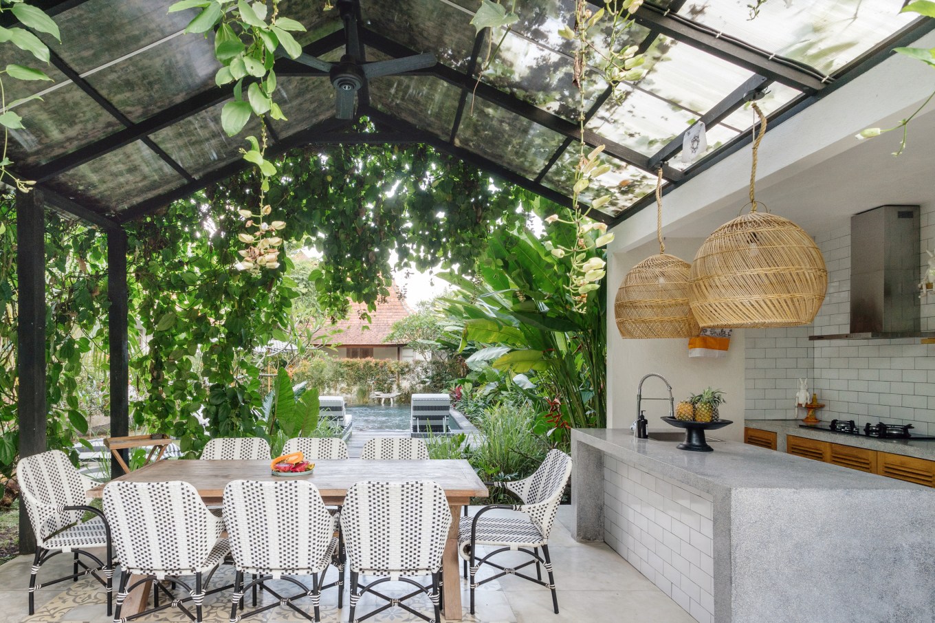 Open outdoor kitchen with a dining room table and chairs outside, with a fan for cooling overhead.