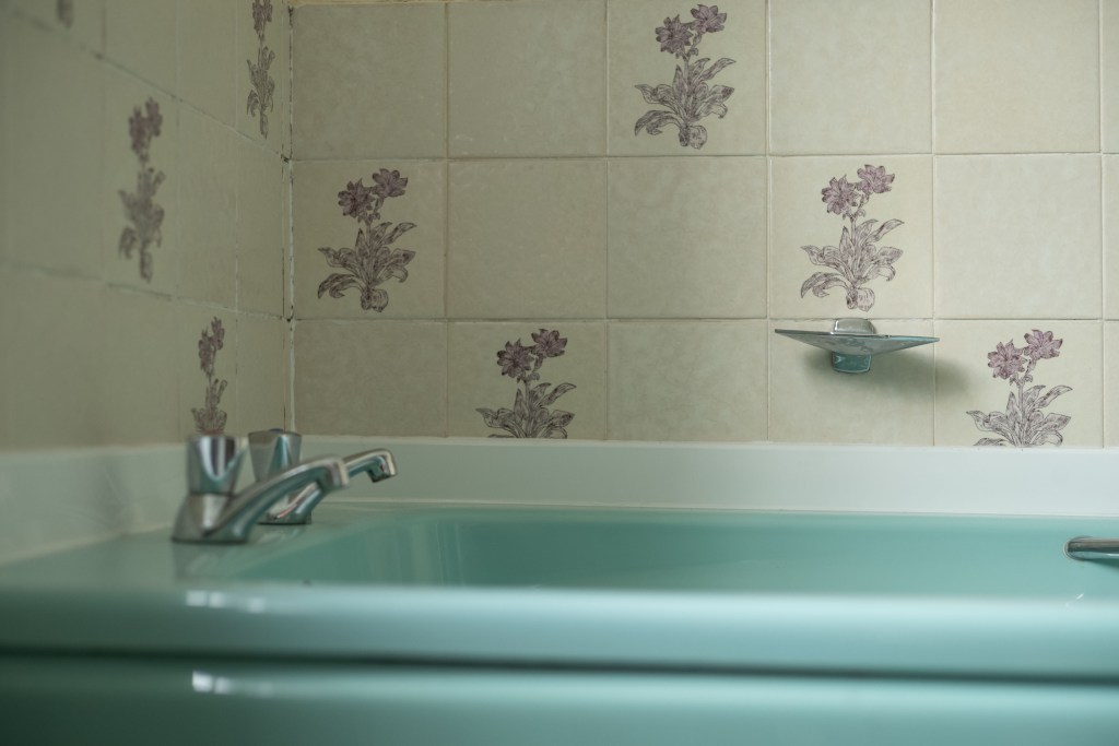 Turquoise bathtub with silver faucet in a vintage bathroom with wall tiling.