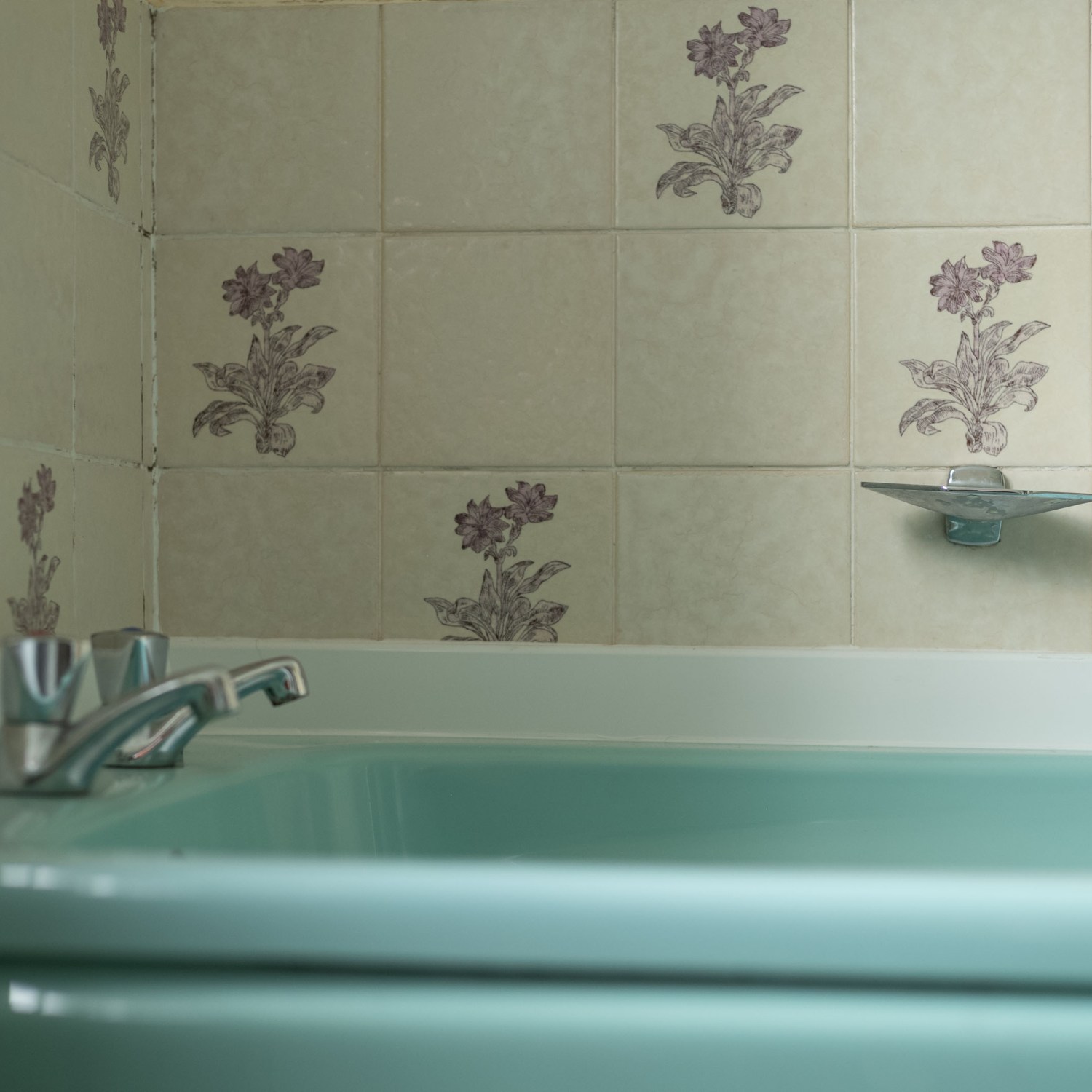 Turquoise bathtub with silver faucet in a vintage bathroom with wall tiling.