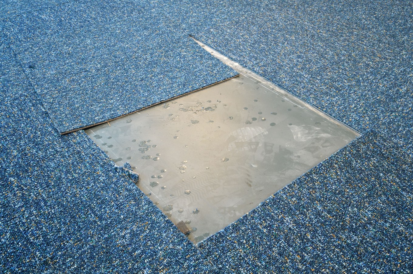 A square section of a blue carpet cut out in the course of carpet installation.