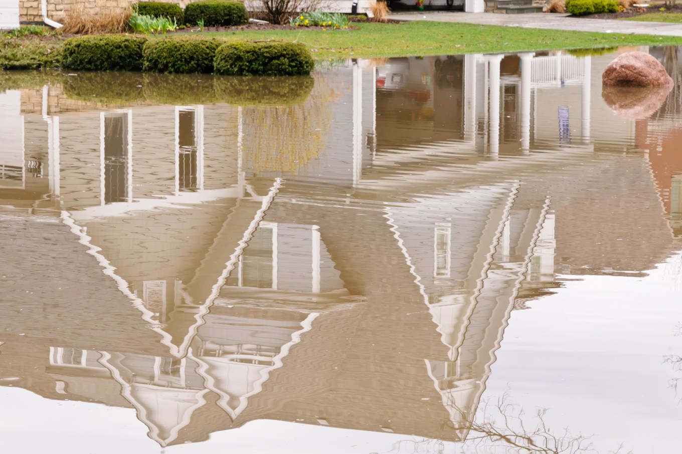 A house reflected in rainwater pooled after a storm due to improper drainage.