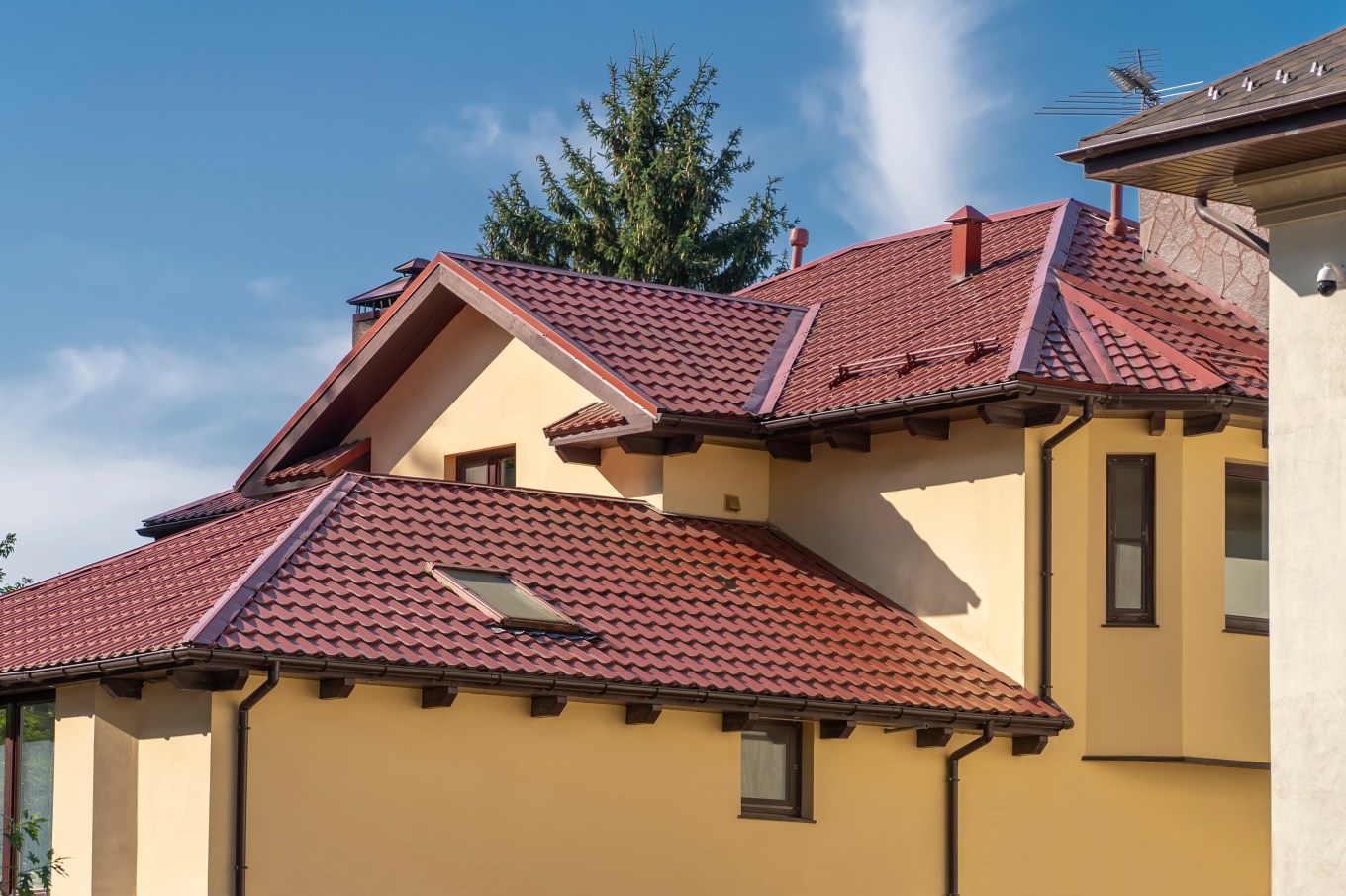 Sloping roof of a cottage made of metal tiles with drains, vents, and a chimney.