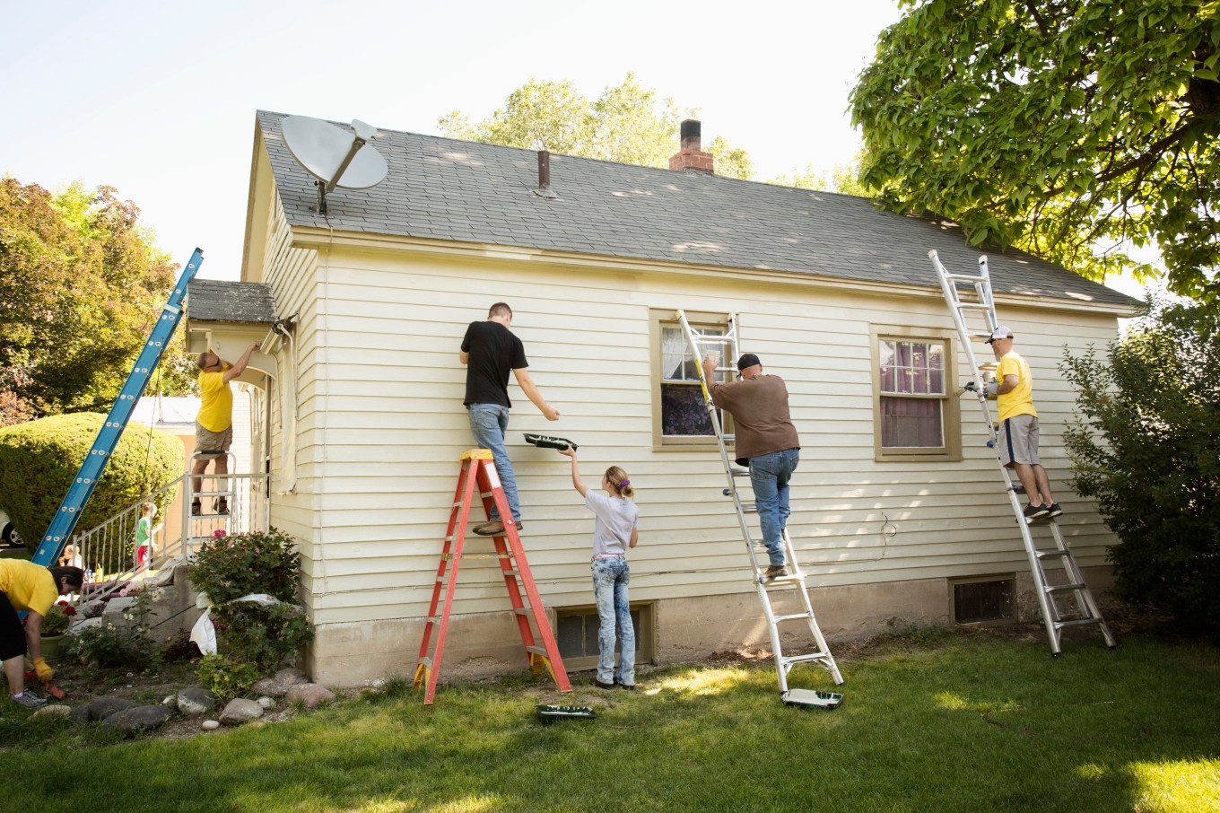 A group of people painting a house on ladders, making it more aesthetically pleasing