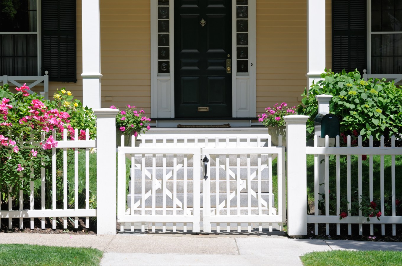 Small white gate and picket fence with roses in front of a porch creates curb appeal