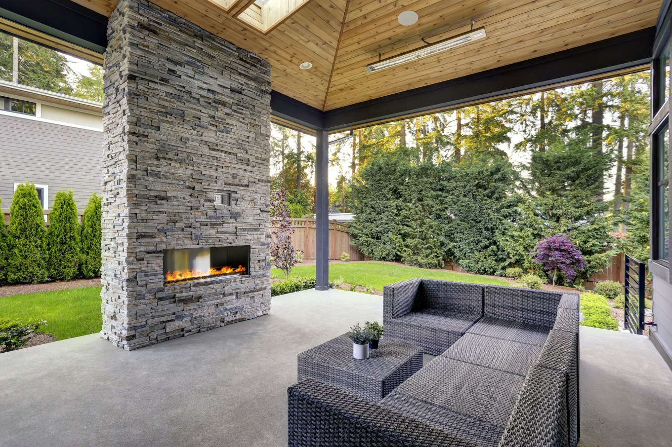 New modern home features a backyard with covered patio accented with stone fireplace and a sofa.