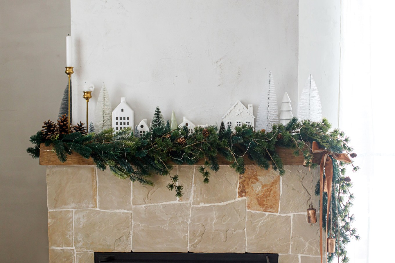 Stylish, modern Christmas fireplace decorated in Scandinavian fashion with trees, houses, pine cones and spruce branches on the mantle.