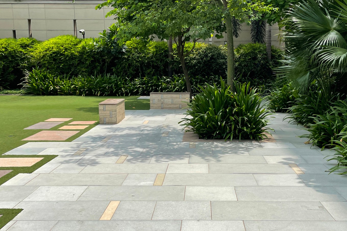 Patio with concrete pavers in varying shapes and sizes with well kept hedges and trees.