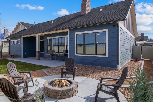 Modern, landscaped, new home with a covered, concrete patio and a fire pit with chairs.