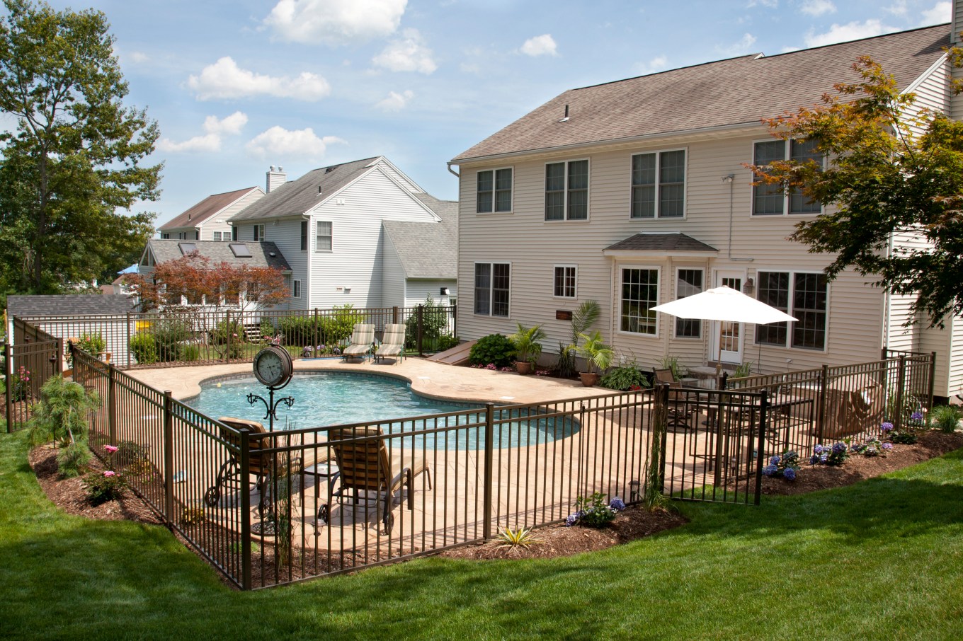 Lush, resort-like backyard swimming pool with a bronze pool fence surrounding it.