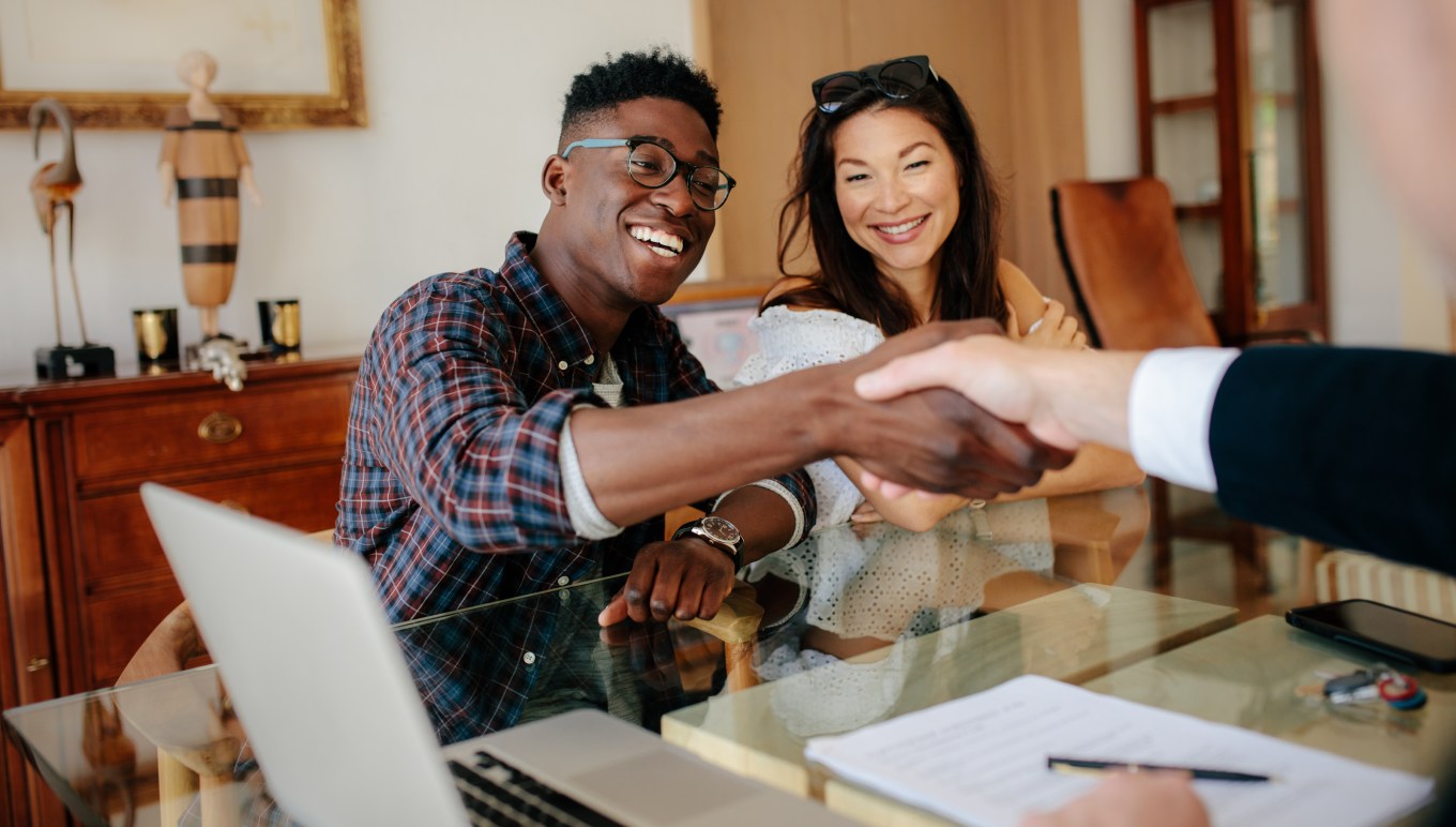 A happy couple shaking the hand of a Real Estate Agent after buying a house.