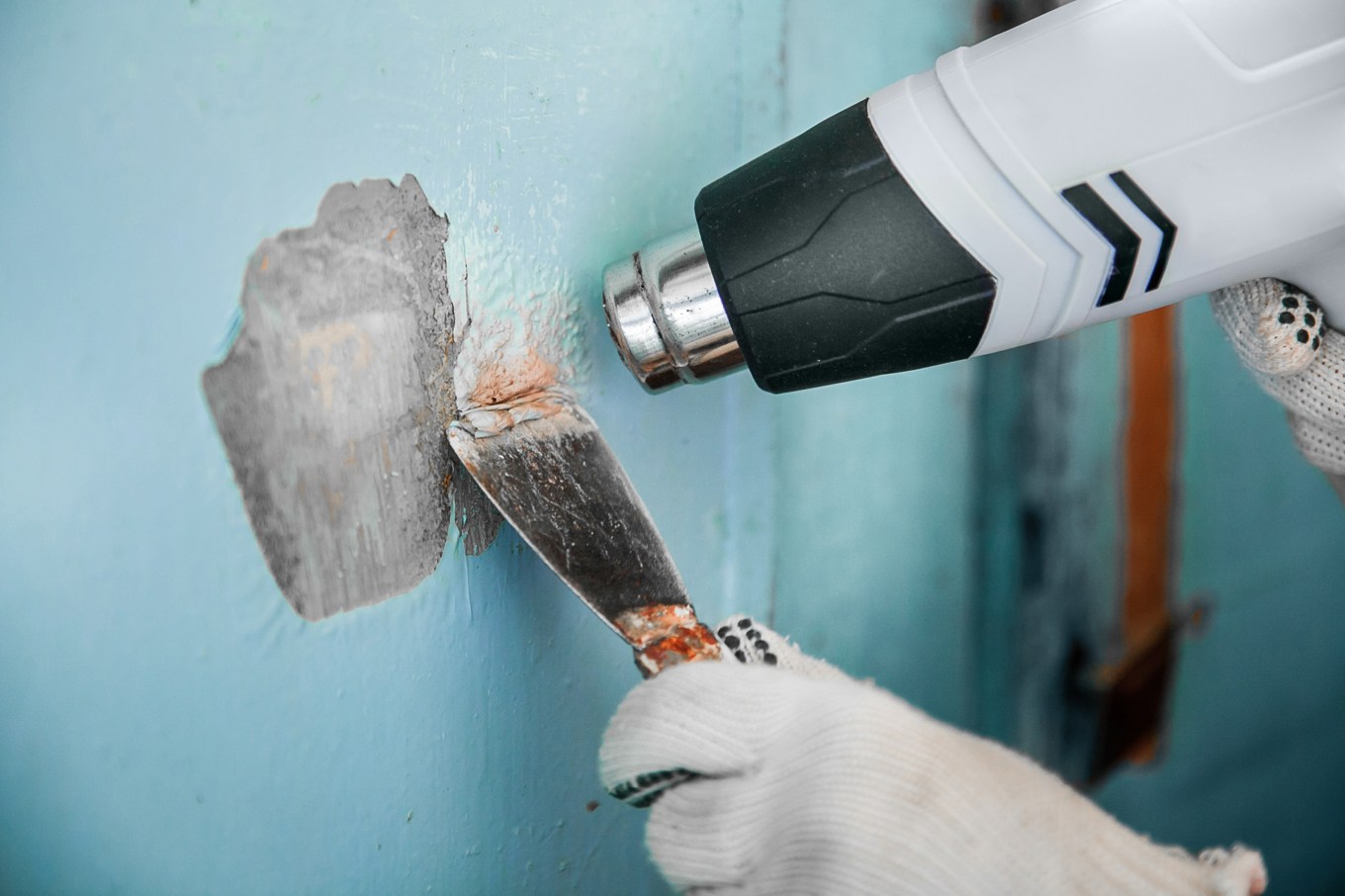 Removing paint from a concrete wall with a scraper and a heat gun.