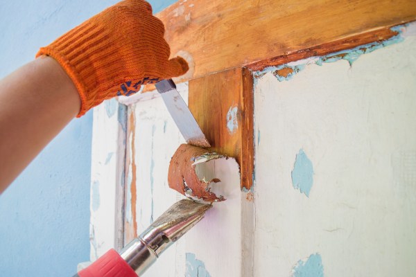 Removing paint from an old, wooden door frame with a scraper and a hair dryer.