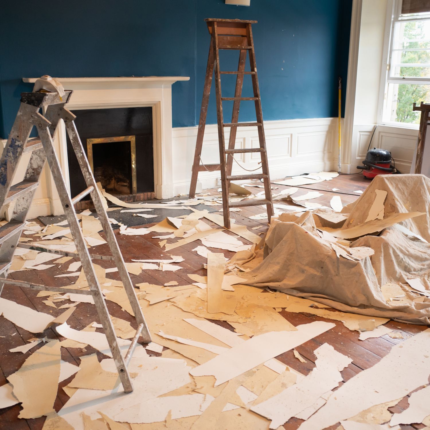 A room in the midst of a renovation, the floor is covered with wallpaper stripped from the walls and ceiling.