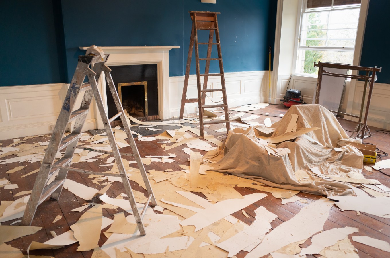 A room in the midst of a renovation, the floor is covered with wallpaper stripped from the walls and ceiling.