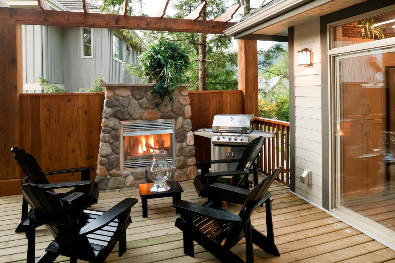 An outdoor fireplace close to a house on a wooden deck.