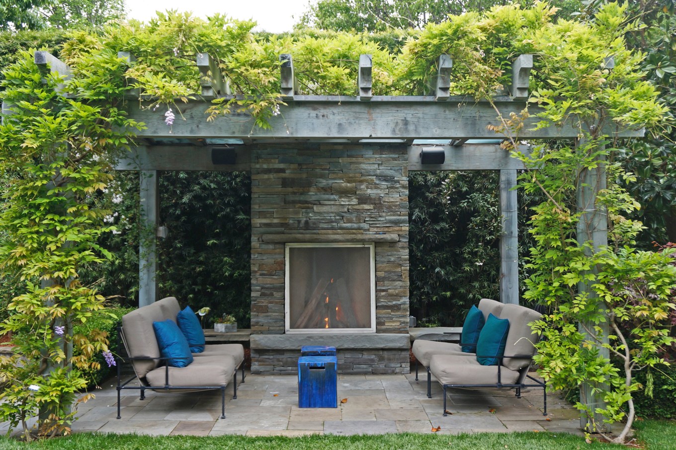 A customized outdoor fireplace with plants growing around it and seating for a few people.