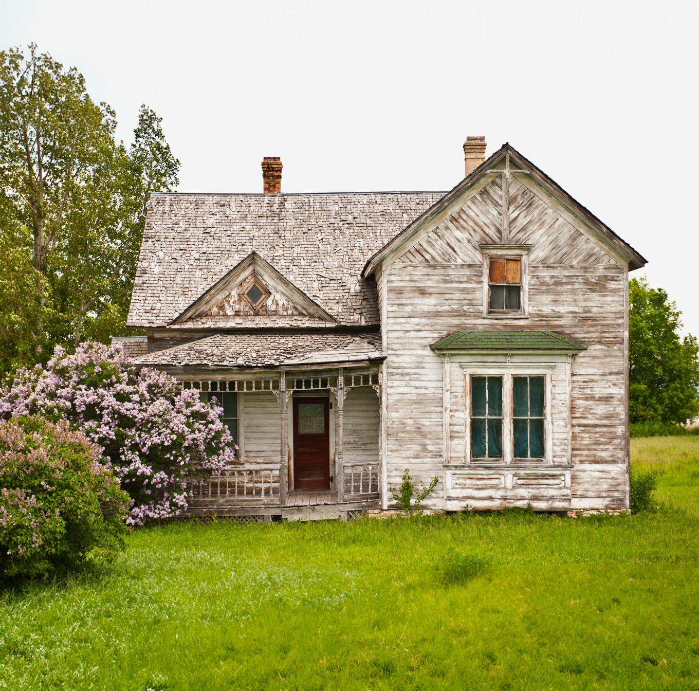 A dilapidated, abandoned fixer-upper house with lots of visible problems sitting in a nice yard with beautiful trees.