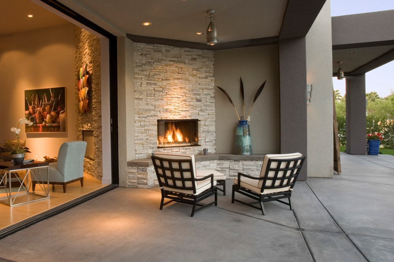 A modern, luxury outdoor fireplace on the patio with two chairs.