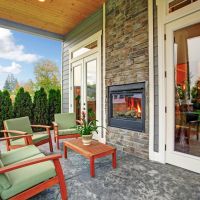 Cozy backyard deck with wooden furniture set and an outdoor fireplace built in the wall.