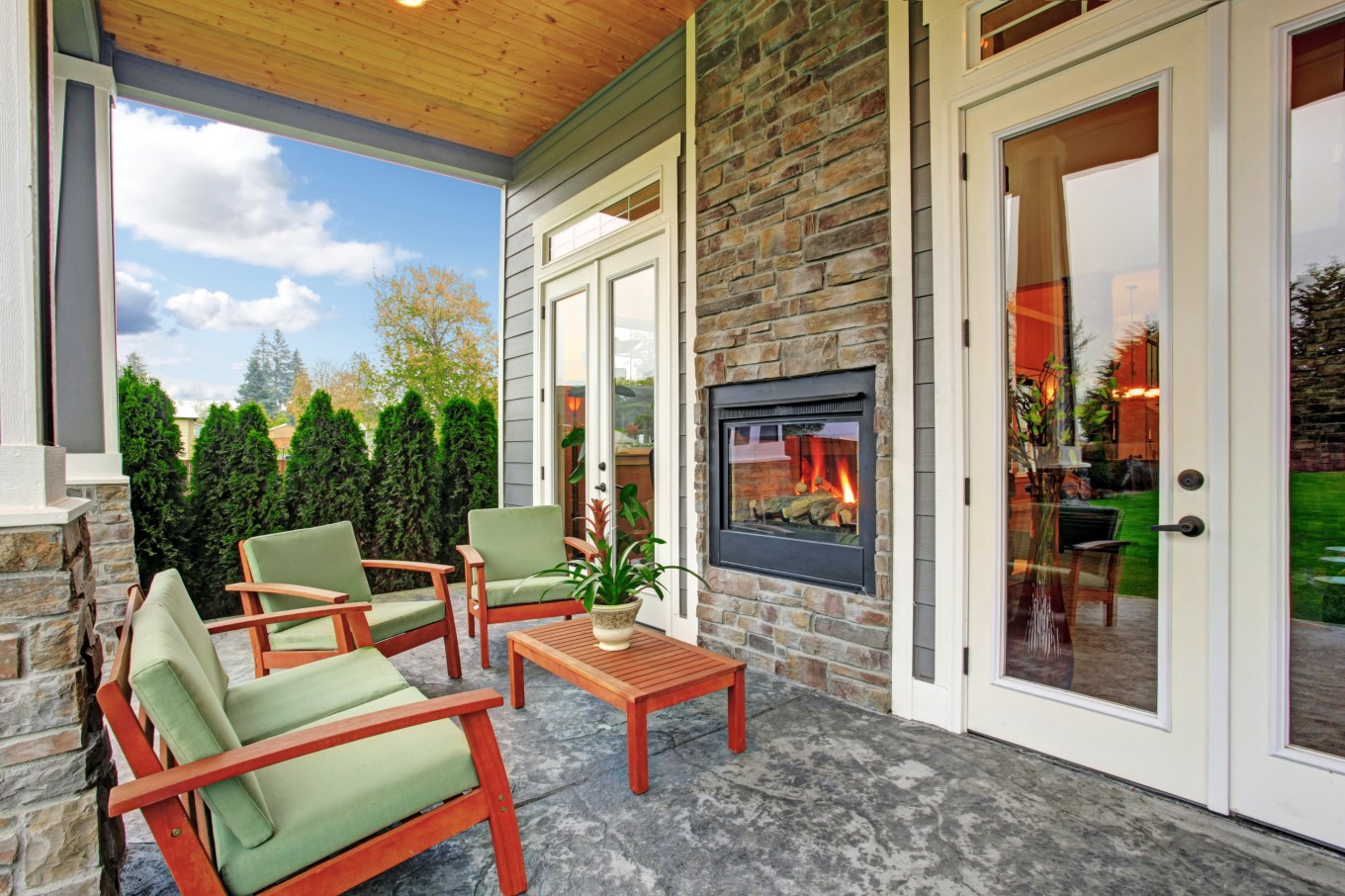 Cozy backyard deck with wooden furniture set and an outdoor fireplace built in the wall.