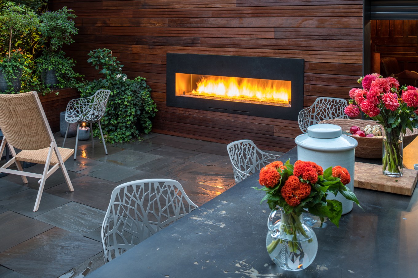 An outdoor fireplace with a backyard garden and a patio with a slated floor.