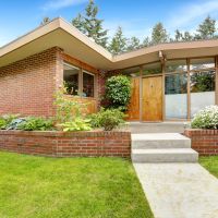 House with brick trim and large windows. Spacious entrance porch and front yard with concrete walkway