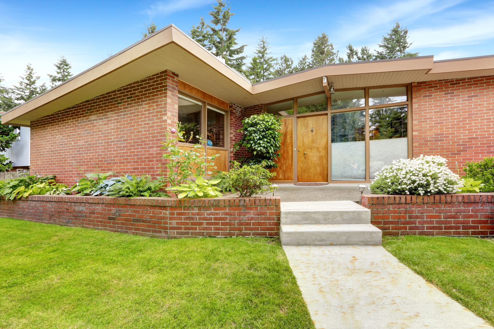 House with brick trim and large windows. Spacious entrance porch and front yard with concrete walkway