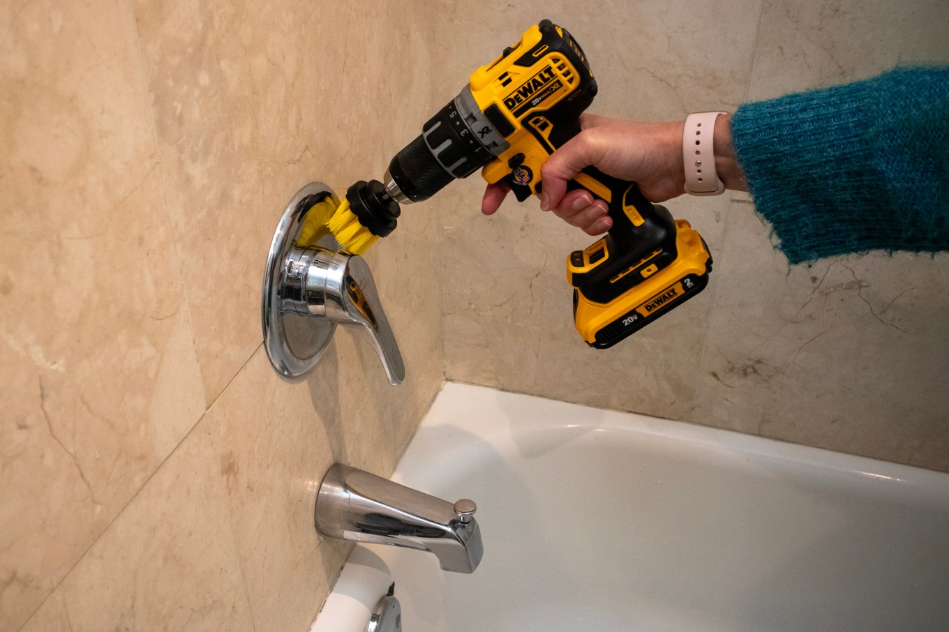 A drill with a cleaning head attachment is used to clean a bathtub.