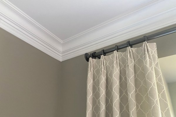 White crown molding joining a wall to the ceiling above a curtained window.