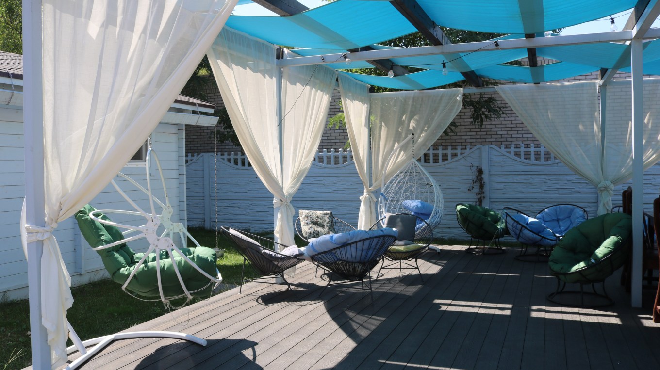 A private relaxation area on the sun terrace with comfortable chairs, light filtering curtains, and wicker swings, the use of light light textiles in the interior design, a cozy veranda.