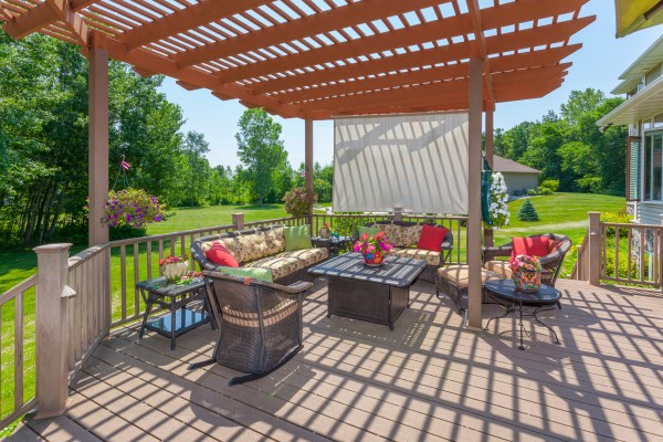 An inviting backyard deck with chairs, a table and a pergola to cover it.
