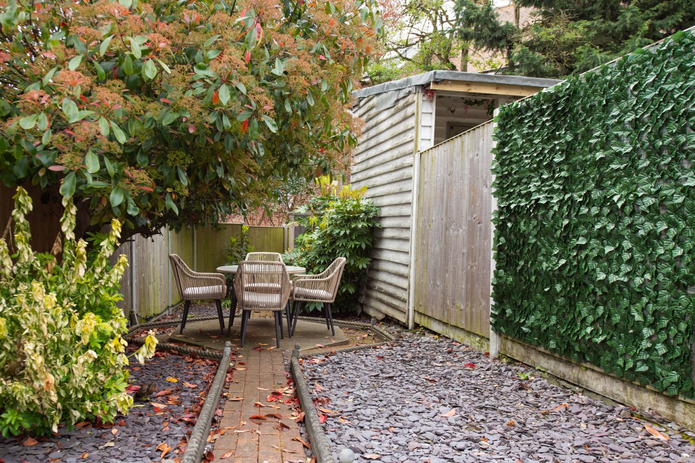 A general view of a small courtyard garden hidden from view by a greenery panel with a cobblestone patio, slate chippings, table and string rope chairs