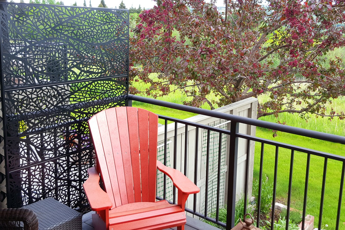 Partial residential deck with black free standing decorative privacy screen that hides the next door neighbor's area that is in close contact. Black iron railing.