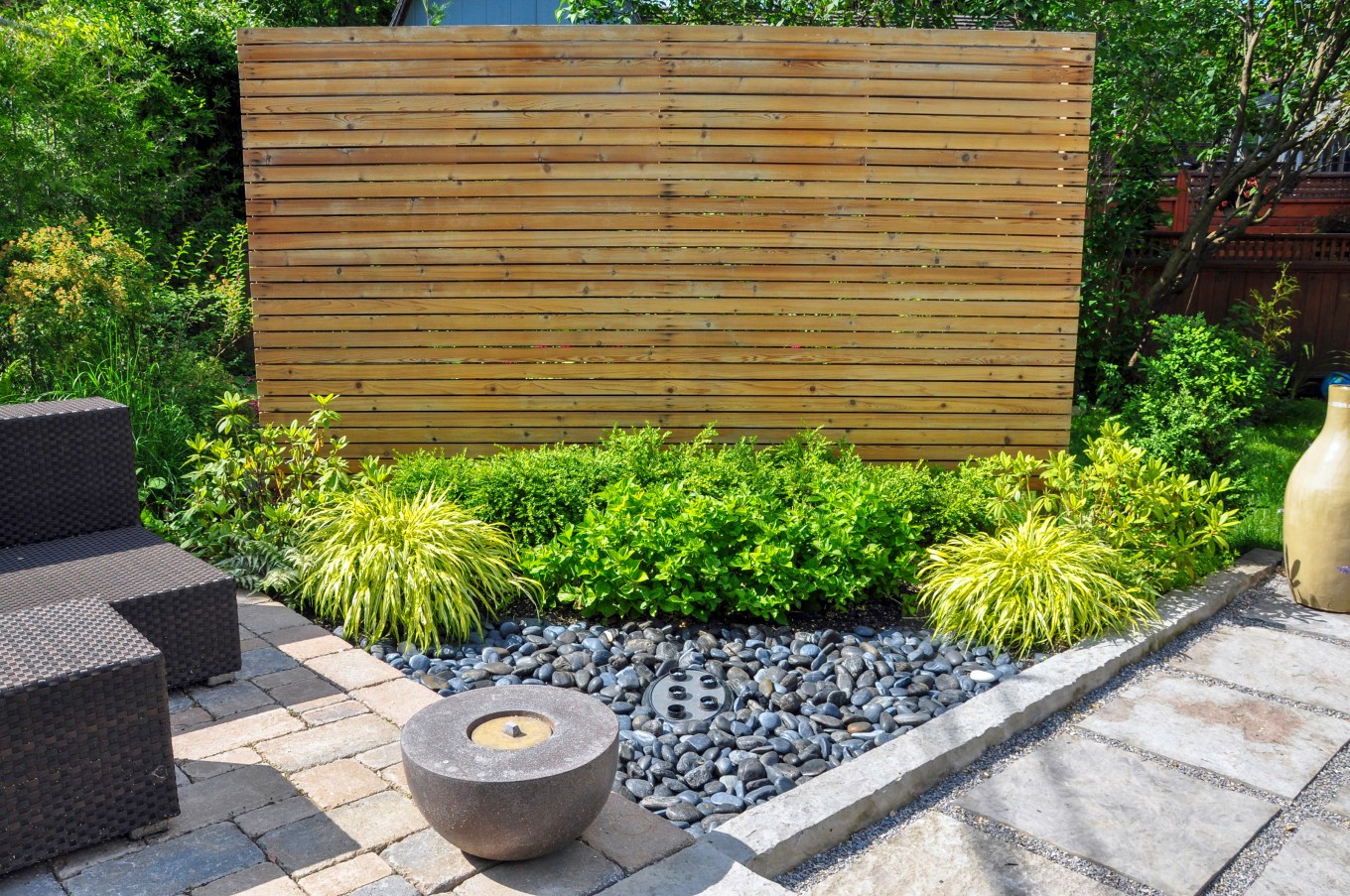 A slatted wooden wall hides the neighbor's from view. Beach pebbles, square cut flagstone and brick landscape pavers and simple plantings provide ample texture and contrast in this small contemporary backyard Asian inspired urban garden.