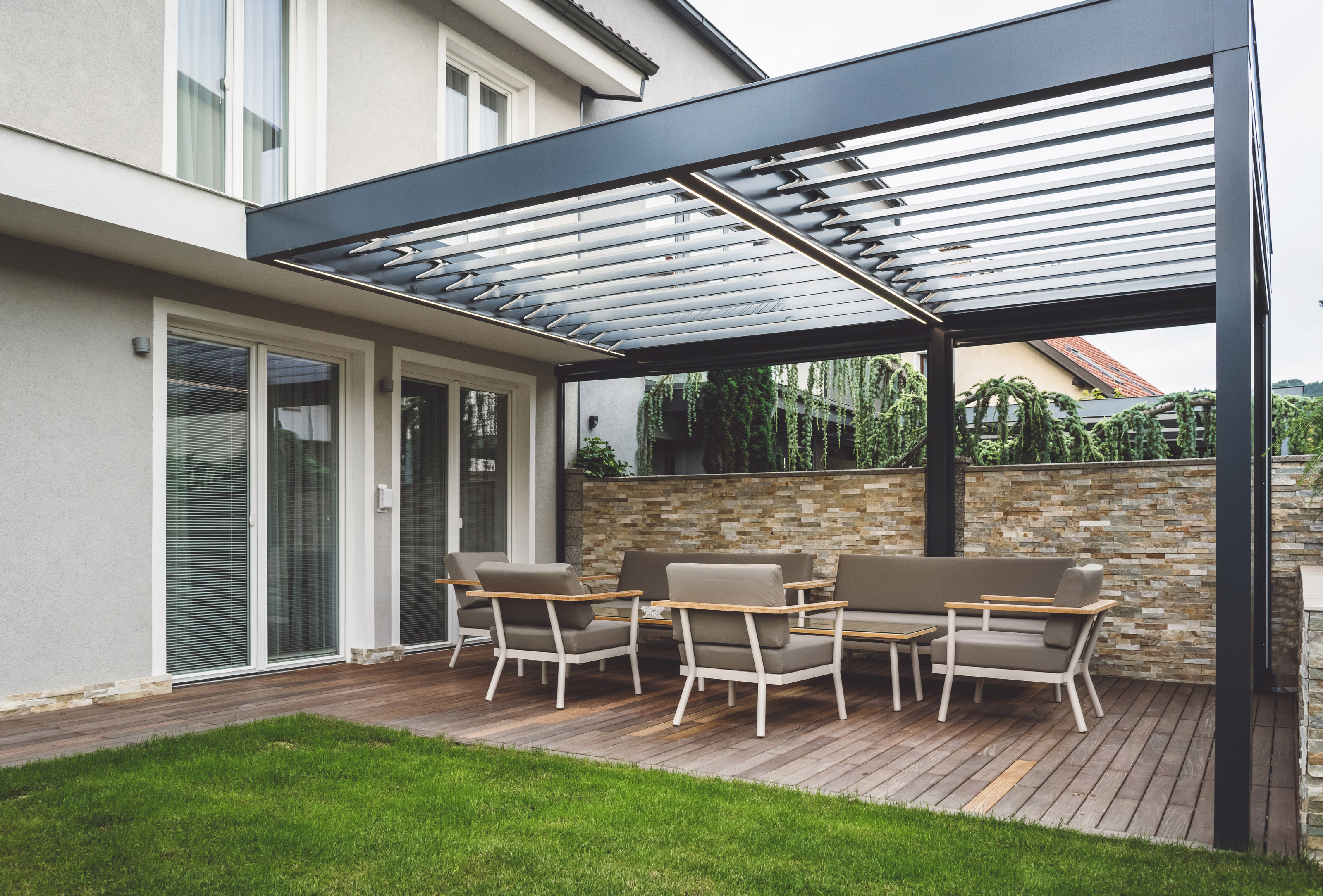 Modern home with attached pergola and a stone wall for privacy.