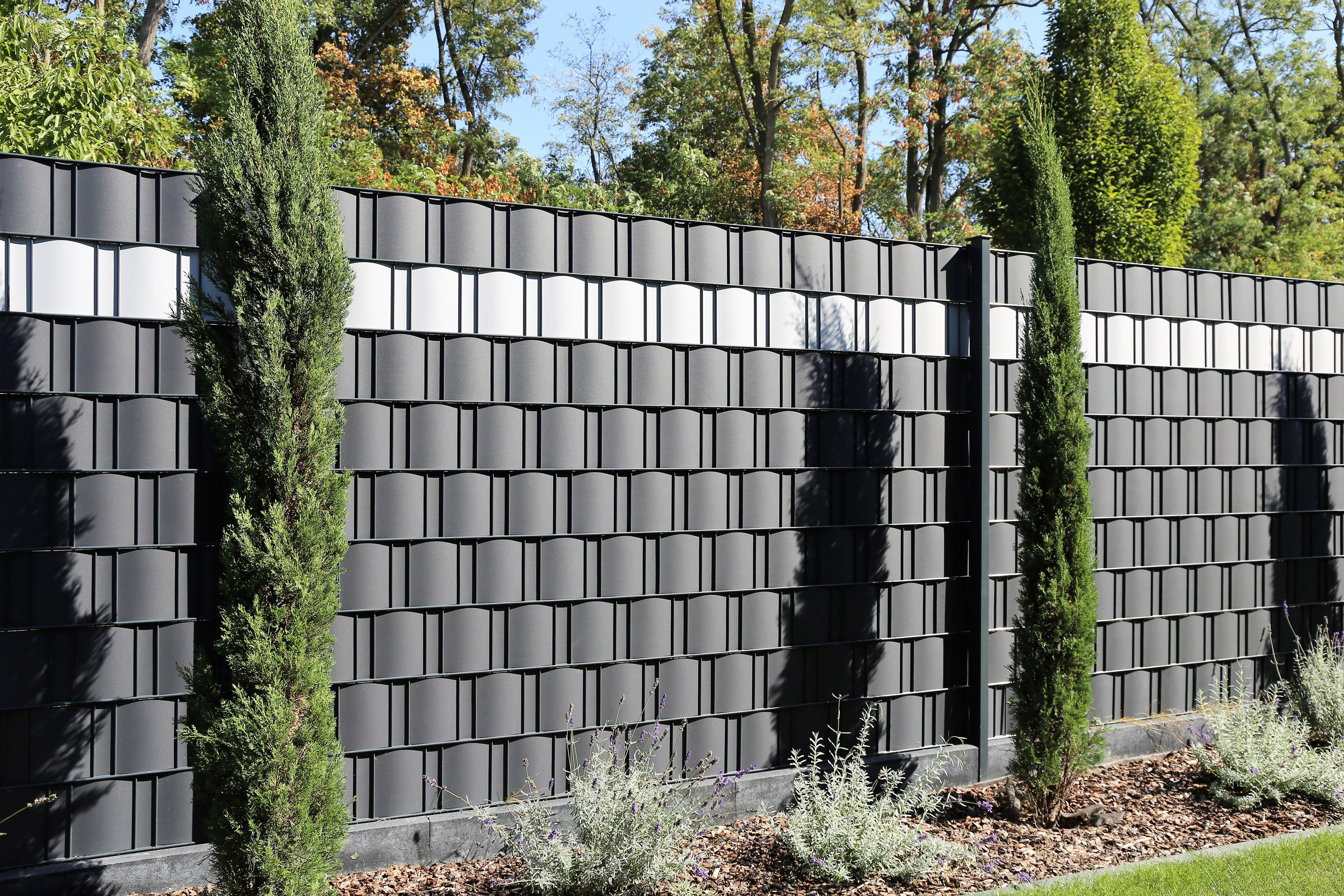 Modern privacy fence with ridged texture and a flower bed in front.