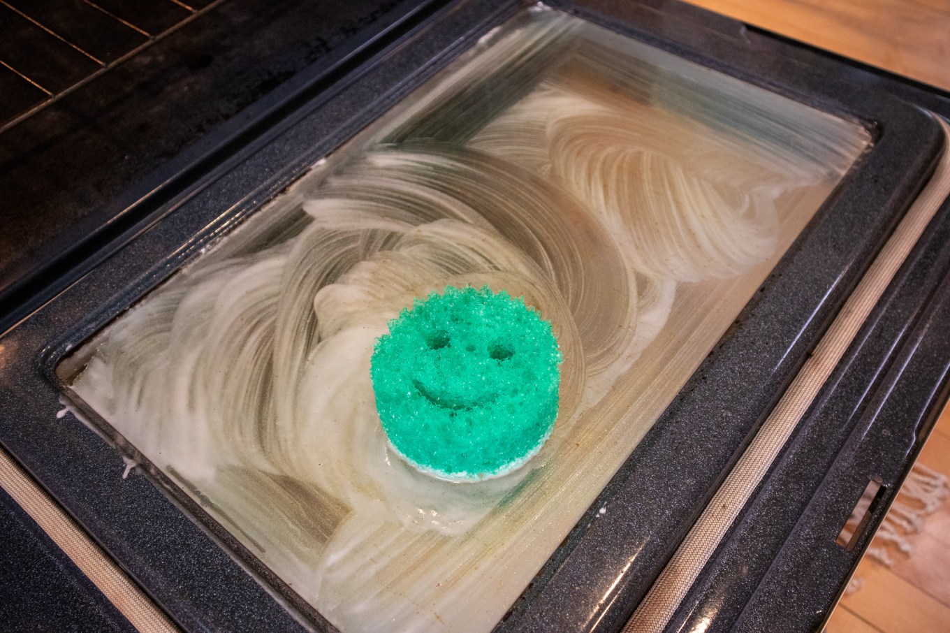 Baking soda mixed with water being spread over the top of an oven with a sponge.