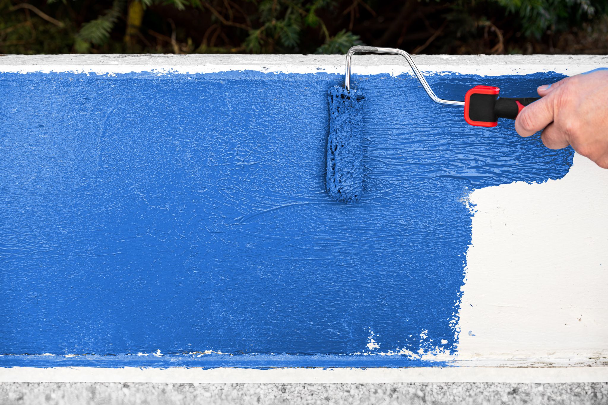 Someone painting a concrete wall with a paint roller and blue paint.